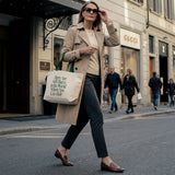Woman walking on a city street wearing a trench coat and carrying a tote bag.